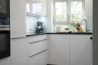 ニュルンベルクにある高級な小さなコンテンポラリースタイルのおしゃれなキッチン (シングルシンク、白いキャビネット、クオーツストーンカウンター、白いキッチンパネル、ガラス板のキッチンパネル、シルバーの調理設備、磁器タイルの床、アイランドなし、グレーの床、黒いキッチンカウンター) の写真