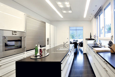 Inspiration pour une grande cuisine parallèle design avec un placard à porte plane, des portes de placard blanches, un électroménager en acier inoxydable, un sol en carrelage de céramique, îlot et un sol noir.
