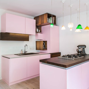 Foto di una cucina eclettica con lavello da incasso, ante lisce, paraspruzzi bianco, parquet chiaro, paraspruzzi con lastra di vetro, penisola, pavimento beige e top rosa