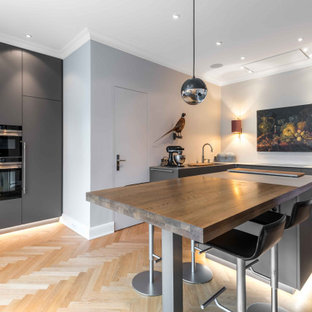 Mittelgroße Moderne Küche in L-Form mit Unterbauwaschbecken, flächenbündigen Schrankfronten, grauen Schränken, Arbeitsplatte aus Holz, Elektrogeräten mit Frontblende, hellem Holzboden, Kücheninsel, beigem Boden und brauner Arbeitsplatte in Hamburg
