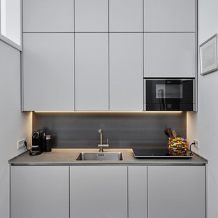 Einzeilige, Kleine Moderne Wohnküche ohne Insel mit Waschbecken, flächenbündigen Schrankfronten, grauen Schränken, Mineralwerkstoff-Arbeitsplatte, Küchenrückwand in Metallic, Rückwand aus Metallfliesen, schwarzen Elektrogeräten, braunem Holzboden und braunem Boden in Düsseldorf