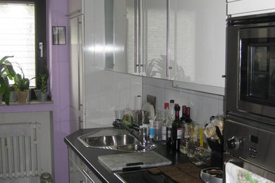 Cette image montre une petite cuisine linéaire design fermée avec un placard à porte plane, des portes de placard blanches et un plan de travail en stratifié.