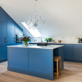 Mittelgroße Klassische Küche in L-Form mit Schrankfronten im Shaker-Stil, blauen Schränken, Küchenrückwand in Weiß, schwarzen Elektrogeräten, Kücheninsel, weißer Arbeitsplatte, Rückwand aus Stein, hellem Holzboden und beigem Boden in München
