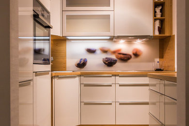 Kleine Moderne Küche in U-Form mit flächenbündigen Schrankfronten, Arbeitsplatte aus Holz, bunter Rückwand und Glasrückwand in Dresden