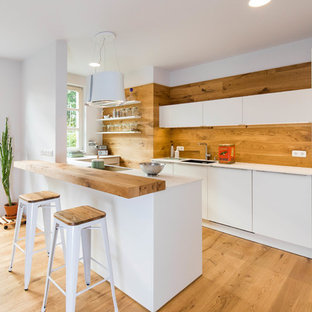 Offene, Mittelgroße Skandinavische Küche in U-Form mit integriertem Waschbecken, flächenbündigen Schrankfronten, weißen Schränken, Küchenrückwand in Braun, Rückwand aus Holz, braunem Holzboden, Halbinsel, braunem Boden, weißer Arbeitsplatte und Elektrogeräten mit Frontblende in Nürnberg