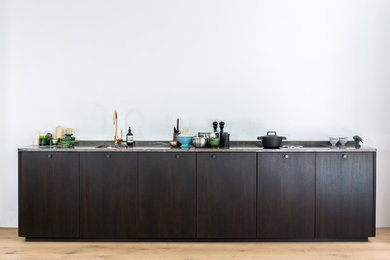 Cette image montre une cuisine ouverte linéaire design en bois foncé avec une crédence blanche et un électroménager noir.