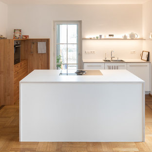 Große, Offene Moderne Küche in L-Form mit flächenbündigen Schrankfronten, Laminat-Arbeitsplatte, Küchenrückwand in Weiß, Küchengeräten aus Edelstahl, weißer Arbeitsplatte, Unterbauwaschbecken, weißen Schränken, braunem Holzboden, Kücheninsel und braunem Boden in Stuttgart