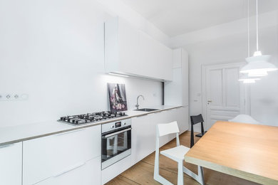 Photo of a medium sized modern single-wall kitchen/diner in Frankfurt with a double-bowl sink, flat-panel cabinets, white cabinets, wood worktops, white splashback, stainless steel appliances, light hardwood flooring, no island, brown floors and white worktops.