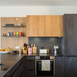 Kleine Moderne Küche in L-Form mit flächenbündigen Schrankfronten, grauen Schränken, Küchenrückwand in Schwarz, Elektrogeräten mit Frontblende, Halbinsel und schwarzer Arbeitsplatte in Köln