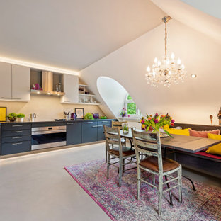 Große Moderne Wohnküche ohne Insel in L-Form mit flächenbündigen Schrankfronten, Mineralwerkstoff-Arbeitsplatte, Küchenrückwand in Beige, schwarzer Arbeitsplatte, grauen Schränken, Betonboden, grauem Boden und gewölbter Decke in München