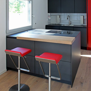 Zweizeilige Moderne Küche mit Waschbecken, flächenbündigen Schrankfronten, schwarzen Schränken, Küchenrückwand in Grau, Glasrückwand, hellem Holzboden, Halbinsel, beigem Boden und schwarzer Arbeitsplatte in Frankfurt am Main