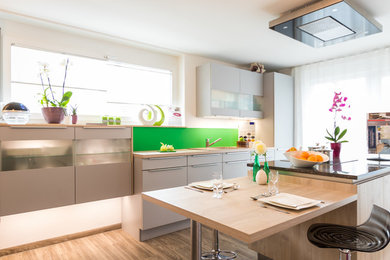 Идея дизайна: параллельная кухня-гостиная среднего размера в современном стиле с накладной мойкой, плоскими фасадами, серыми фасадами, деревянной столешницей, зеленым фартуком, паркетным полом среднего тона, двумя и более островами и коричневым полом