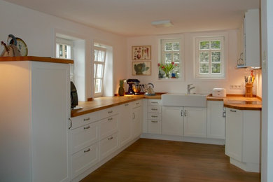 На фото: п-образная кухня-гостиная среднего размера в стиле кантри с с полувстраиваемой мойкой (с передним бортиком), фасадами с декоративным кантом, деревянной столешницей и паркетным полом среднего тона