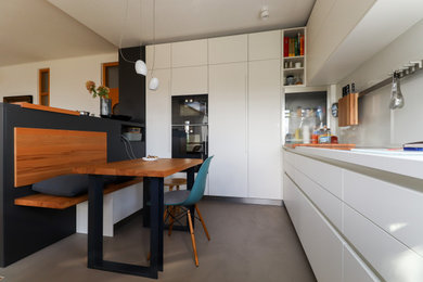 Offene Moderne Küche mit weißen Schränken, Küchenrückwand in Weiß, Glasrückwand, schwarzen Elektrogeräten, Betonboden und grauem Boden in Sonstige