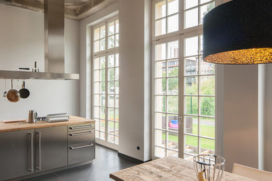 Industrial Wohnküche mit flächenbündigen Schrankfronten, Edelstahlfronten, Arbeitsplatte aus Holz, Schieferboden und Kücheninsel in Leipzig