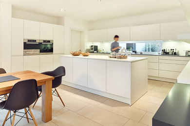 Medium sized scandi l-shaped open plan kitchen in Nuremberg with flat-panel cabinets, white cabinets, stainless steel appliances, cement flooring, multiple islands and beige floors.