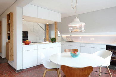 Offene, Zweizeilige Moderne Küche mit weißen Schränken, Zementfliesen für Boden, Kücheninsel, rotem Boden und weißer Arbeitsplatte in Stuttgart