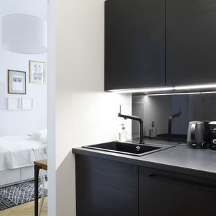 This is an example of a small modern single-wall separate kitchen in Berlin with an integrated sink, louvered cabinets, black cabinets, laminate benchtops, black splashback, metal splashback, black appliances, medium hardwood floors, no island and brown floor.