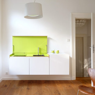 Modelo de cocina lineal, moderna, pequeña, abierta, con fregadero de un seno, armarios con paneles lisos, puertas de armario blancas, suelo de madera en tonos medios y una isla