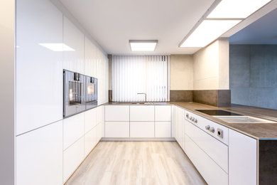 Medium sized modern u-shaped open plan kitchen in Hamburg with flat-panel cabinets, white cabinets, stainless steel appliances, a breakfast bar and light hardwood flooring.
