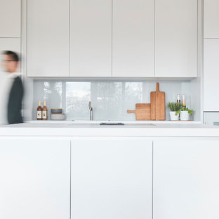 Moderne Küche mit flächenbündigen Schrankfronten, weißen Schränken, Quarzwerkstein-Arbeitsplatte, Küchenrückwand in Grau, Glasrückwand, weißen Elektrogeräten, hellem Holzboden, Kücheninsel, weißer Arbeitsplatte, Unterbauwaschbecken und beigem Boden in Hamburg