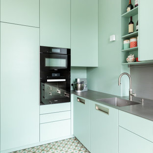 This is an example of a small contemporary l-shaped separate kitchen in Frankfurt with an integrated sink, flat-panel cabinets, green cabinets, stainless steel benchtops, grey splashback, metal splashback, black appliances, turquoise floor, grey benchtop and no island.