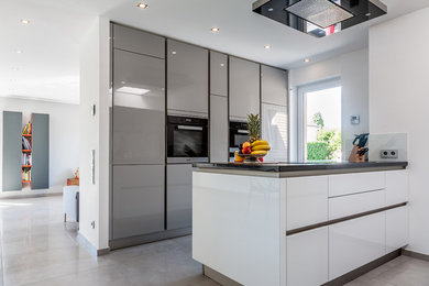 Modelo de cocina contemporánea pequeña abierta con armarios con paneles lisos, electrodomésticos negros, península, suelo gris, encimeras negras y puertas de armario grises