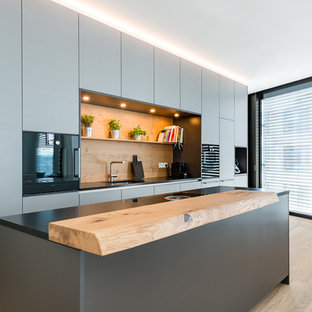Esempio di una piccola cucina design con ante grigie, paraspruzzi in legno, elettrodomestici neri, pavimento marrone, top nero, lavello sottopiano, ante lisce, top in granito, paraspruzzi marrone, pavimento in legno massello medio e isola
