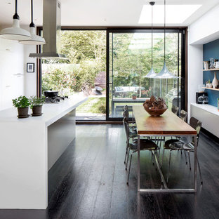 Mittelgroße Moderne Wohnküche mit dunklem Holzboden, braunem Boden, flächenbündigen Schrankfronten, weißen Schränken, Küchengeräten aus Edelstahl, Kücheninsel und weißer Arbeitsplatte in Hamburg