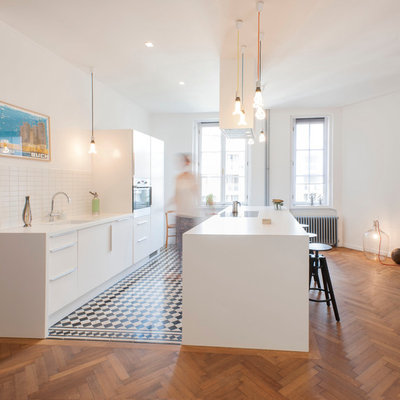 Large trendy single-wall medium tone wood floor eat-in kitchen photo in Munich with flat-panel cabinets, white cabinets, white backsplash, an island, an undermount sink, ceramic backsplash and paneled appliances