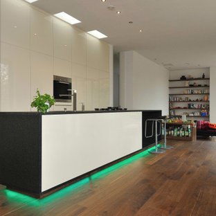 Zweizeilige, Große Moderne Wohnküche mit Unterbauwaschbecken, flächenbündigen Schrankfronten, beigen Schränken, Elektrogeräten mit Frontblende, braunem Holzboden, Kücheninsel, braunem Boden und schwarzer Arbeitsplatte in Stuttgart