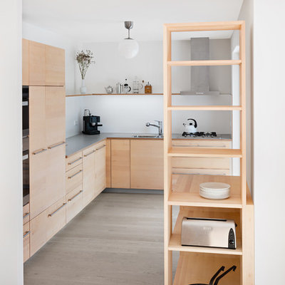 Example of a mid-sized trendy l-shaped light wood floor and beige floor open concept kitchen design in Stuttgart with flat-panel cabinets, light wood cabinets, laminate countertops, gray countertops, white backsplash, paneled appliances, a drop-in sink and no island