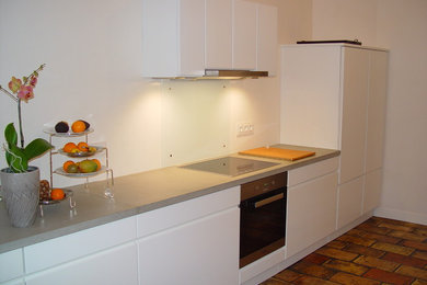 Mittelgroße Moderne Wohnküche mit Betonarbeitsplatte, Küchenrückwand in Weiß, Glasrückwand, Küchengeräten aus Edelstahl und Terrakottaboden in Frankfurt am Main