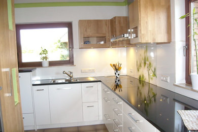 Example of a mid-sized trendy enclosed kitchen design in Stuttgart with flat-panel cabinets, medium tone wood cabinets, granite countertops, white backsplash and glass sheet backsplash