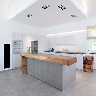 Moderne Küche mit Waschbecken, flächenbündigen Schrankfronten, weißen Schränken, Küchengeräten aus Edelstahl, Betonboden, Kücheninsel, grauem Boden und schwarzer Arbeitsplatte in München
