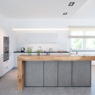 Moderne Küche in L-Form mit Einbauwaschbecken, flächenbündigen Schrankfronten, weißen Schränken, Arbeitsplatte aus Holz, Küchenrückwand in Weiß, schwarzen Elektrogeräten, Kücheninsel, grauem Boden und brauner Arbeitsplatte in München