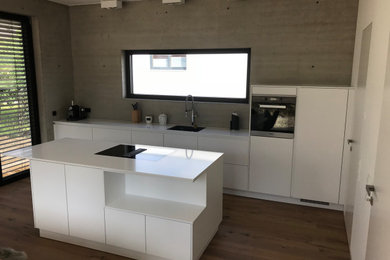 Moderne Küche in grau-weiß mit weißen Schränken, Küchenrückwand in Grau, Laminat, Kücheninsel, braunem Boden und weißer Arbeitsplatte in Sonstige