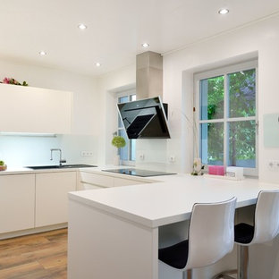 Offene, Kleine Moderne Küche in U-Form mit Einbauwaschbecken, flächenbündigen Schrankfronten, weißen Schränken, Küchenrückwand in Weiß, Glasrückwand, braunem Holzboden, Halbinsel, braunem Boden und weißer Arbeitsplatte in Nürnberg