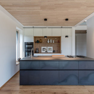 Zweizeilige Moderne Küche mit integriertem Waschbecken, flächenbündigen Schrankfronten, weißen Schränken, Küchenrückwand in Braun, Rückwand aus Holz, schwarzen Elektrogeräten, braunem Holzboden, Kücheninsel, braunem Boden und grauer Arbeitsplatte in München