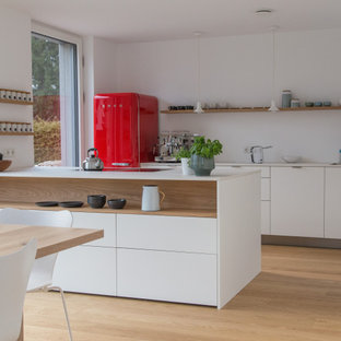 Zweizeilige Moderne Küche mit Unterbauwaschbecken, flächenbündigen Schrankfronten, weißen Schränken, bunten Elektrogeräten, braunem Holzboden, Halbinsel, braunem Boden und weißer Arbeitsplatte in München