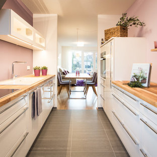 Réalisation d'une cuisine parallèle design fermée et de taille moyenne avec un évier posé, un placard à porte plane, des portes de placard blanches, un plan de travail en bois, un électroménager encastrable, aucun îlot et une crédence rose.