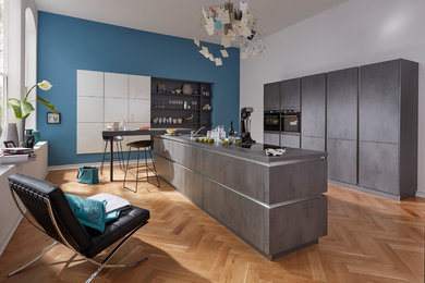 Diseño de cocina lineal contemporánea de tamaño medio con salpicadero azul, electrodomésticos negros, suelo de madera en tonos medios, una isla y puertas de armario grises
