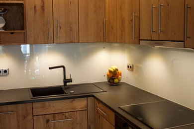 フランクフルトにある中くらいなコンテンポラリースタイルのおしゃれなキッチン (シングルシンク、御影石カウンター、白いキッチンパネル、ガラス板のキッチンパネル、シルバーの調理設備、淡色無垢フローリング) の写真
