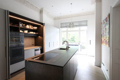 Geschlossene, Einzeilige, Mittelgroße Moderne Küche mit integriertem Waschbecken, flächenbündigen Schrankfronten, schwarzen Elektrogeräten, zwei Kücheninseln, braunem Boden und schwarzer Arbeitsplatte in Hamburg