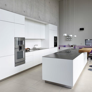 Moderne Wohnküche mit Waschbecken, flächenbündigen Schrankfronten, weißen Schränken, Küchenrückwand in Weiß, Küchengeräten aus Edelstahl, Kücheninsel, beigem Boden und grauer Arbeitsplatte in Bremen