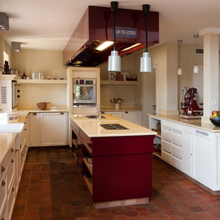 Offene, Mittelgroße Country Küche in U-Form mit Landhausspüle, Schrankfronten mit vertiefter Füllung, weißen Schränken, Küchenrückwand in Beige, Küchengeräten aus Edelstahl, Backsteinboden, zwei Kücheninseln und rotem Boden in Berlin