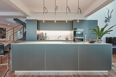 Offene, Einzeilige Moderne Küche mit grauen Schränken, Küchenrückwand in Weiß, schwarzen Elektrogeräten, braunem Holzboden, Kücheninsel und braunem Boden in Hannover