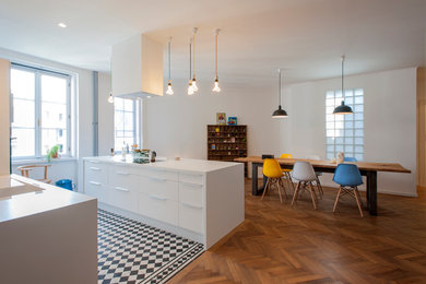Moderne Wohnküche mit flächenbündigen Schrankfronten, weißen Schränken, braunem Holzboden und Kücheninsel in Sonstige