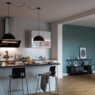 Geräumige, Offene, Zweizeilige Moderne Küche mit braunem Holzboden, braunem Boden, Einbauwaschbecken, flächenbündigen Schrankfronten, weißen Schränken, Küchenrückwand in Weiß, Küchengeräten aus Edelstahl, Kücheninsel, schwarzer Arbeitsplatte, Marmor-Arbeitsplatte und Rückwand aus Zementfliesen in Berlin