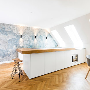 Große Skandinavische Wohnküche in L-Form mit flächenbündigen Schrankfronten, weißen Schränken, Arbeitsplatte aus Holz, hellem Holzboden, Kücheninsel, beigem Boden, beiger Arbeitsplatte, bunter Rückwand und Küchengeräten aus Edelstahl in München